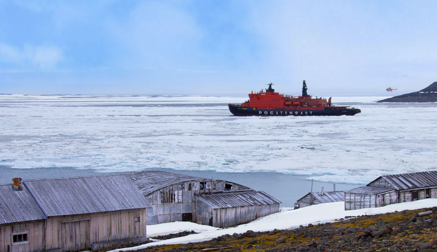 Icebreaker ship in Arctic waters with small wooden huts in the foreground