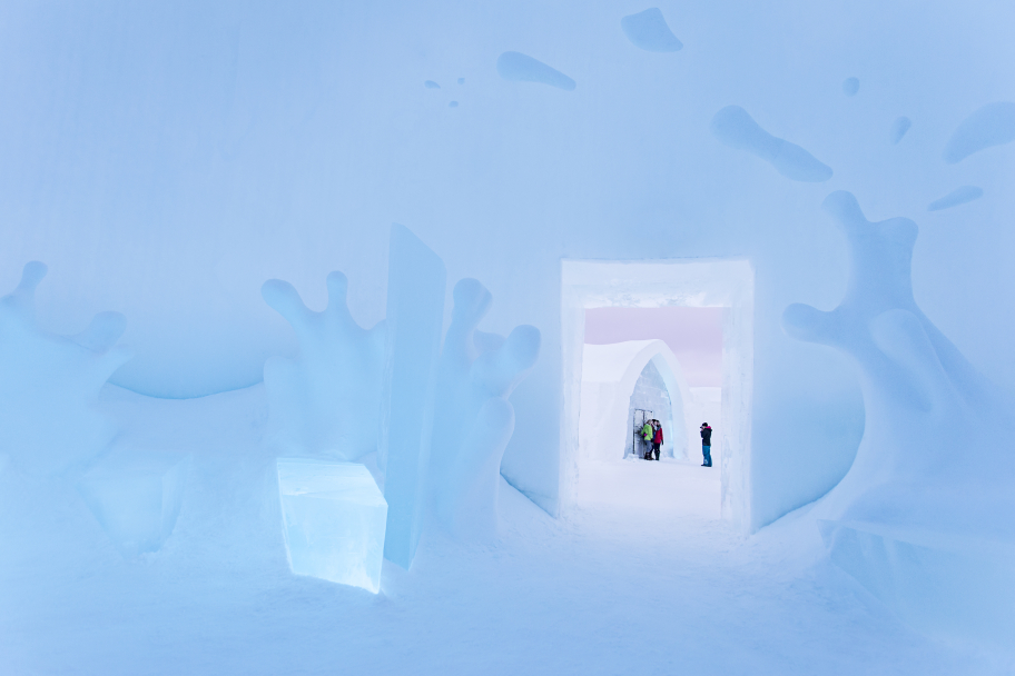 Blue-lit ice hotel interior with sculpted ice features and arched doorway