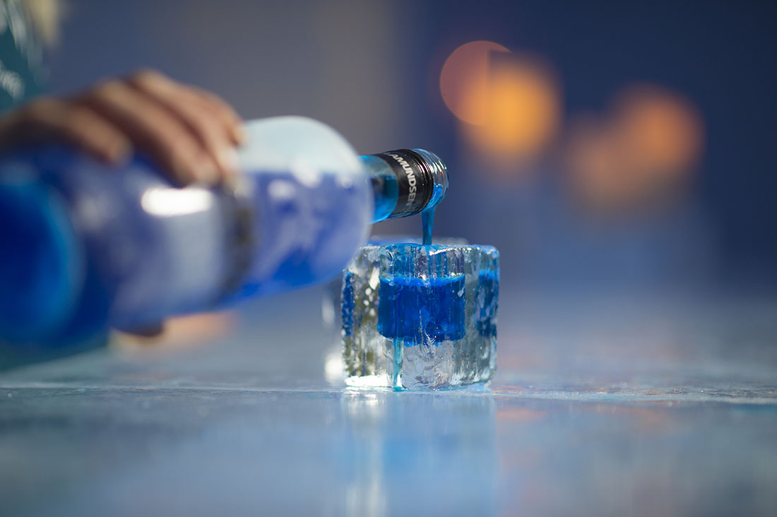 Blue coloured alcohol being poured into an ice glass inside an ice bar setting