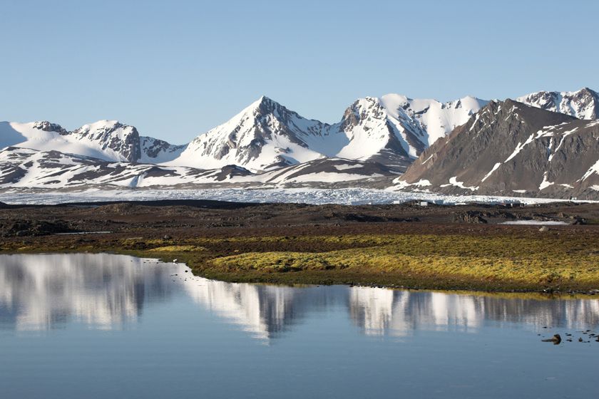 Colourful boats and cabins in a Spitsbergen fjord with mountains under summer light