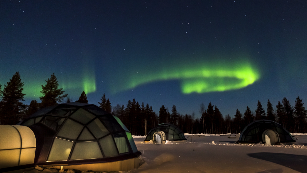 Glass igloo cabins under the northern lights in a snowy landscape
