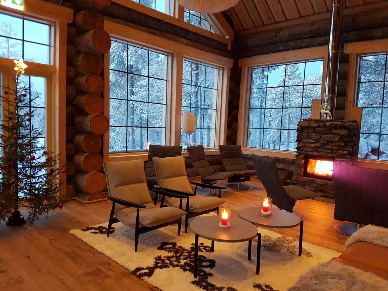 Warm lodge lounge with fireplace, armchairs and large windows looking onto snow