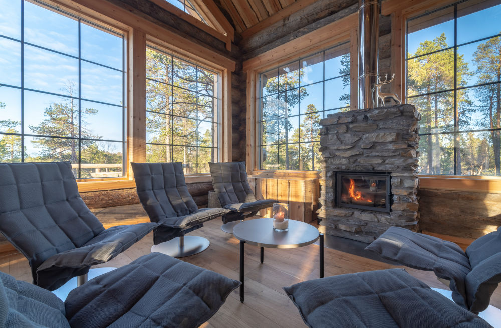 lounge chairs surrounding a small table by the fireplace with large windows overlooking the trees