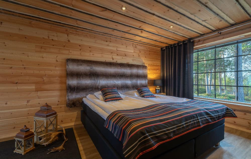 double bed in a log cabin with a large window with a view of the trees on a summer day