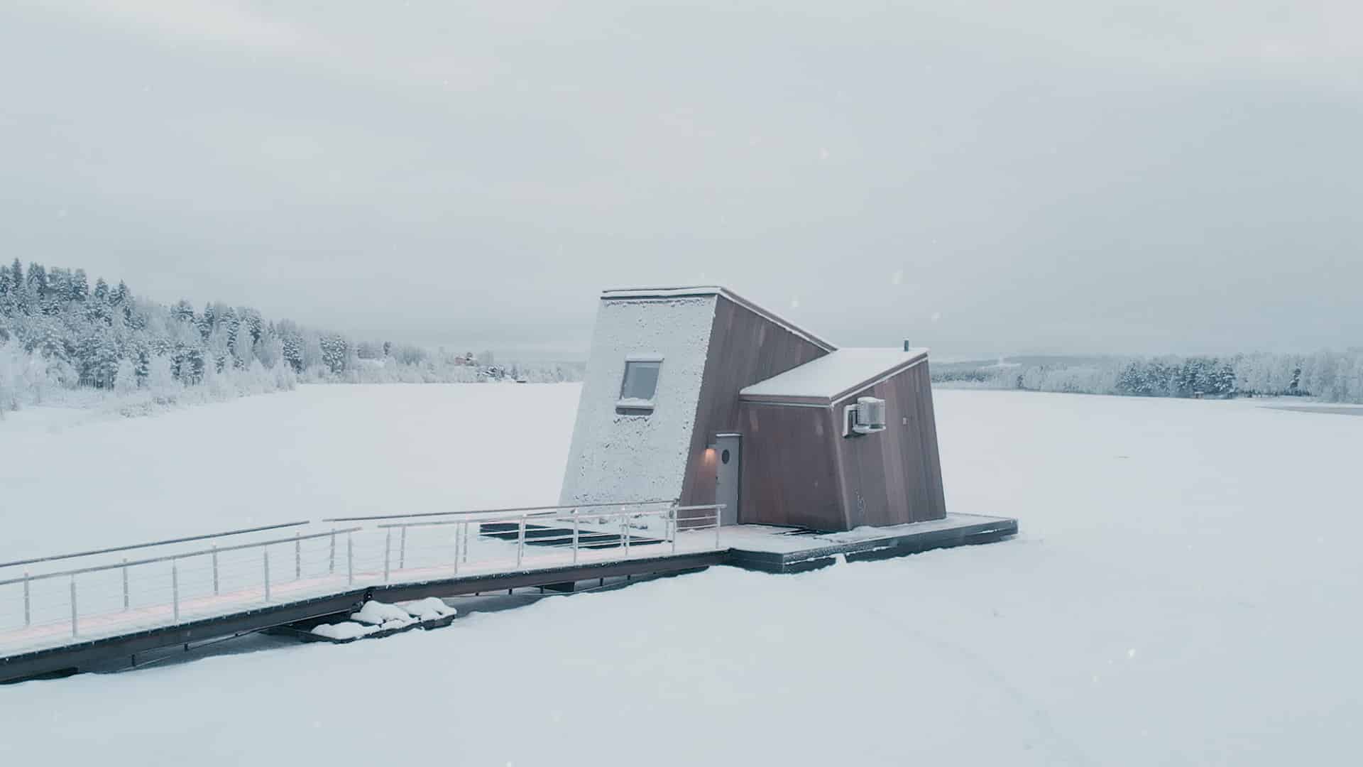 Modern sauna/spa building on a frozen lake with walkway and snow around it