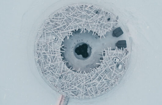 Aerial view of the circular Arctic Bath structure on a frozen river/lake
