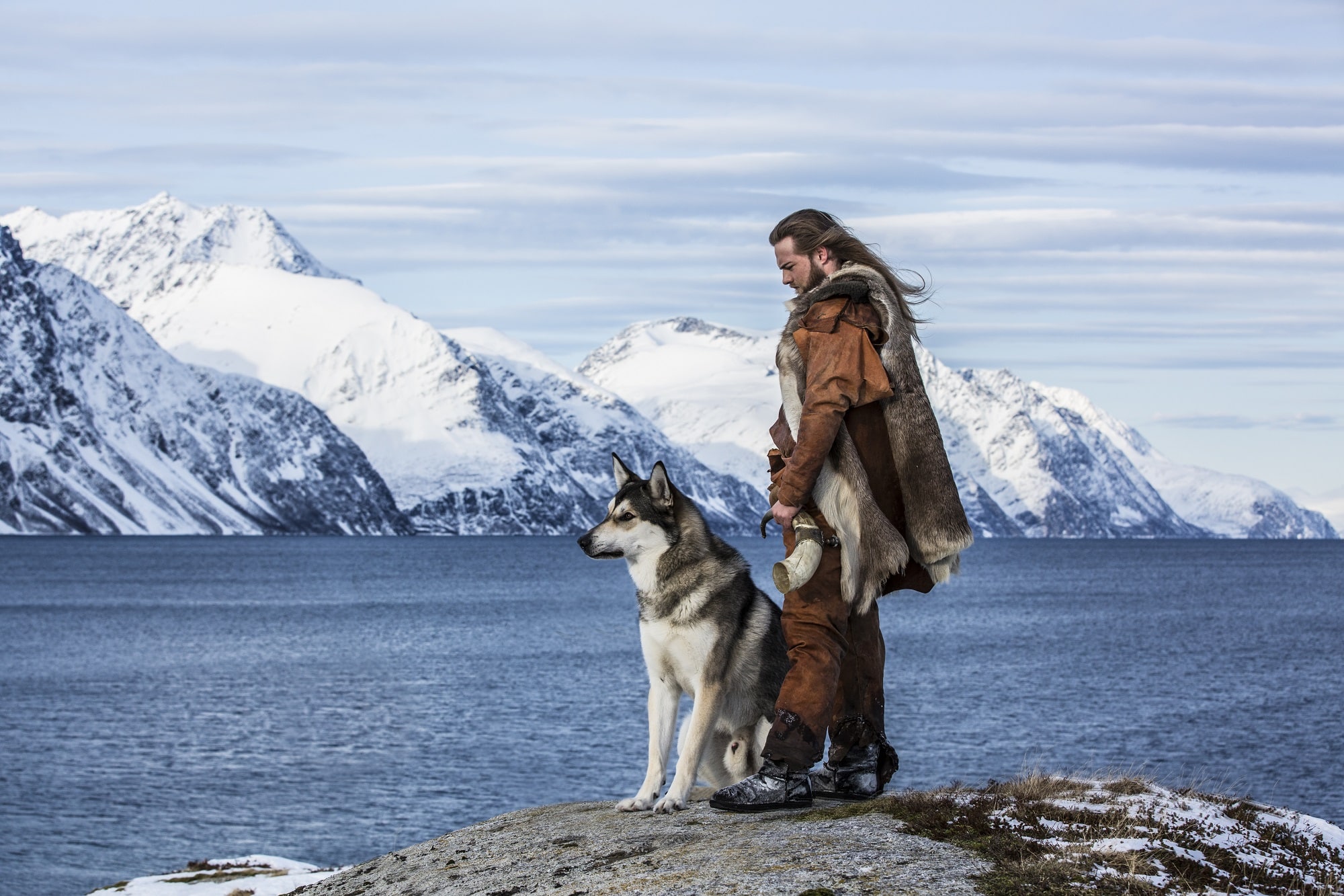 Person with a husky dog standing on a rocky viewpoint with mountains behind