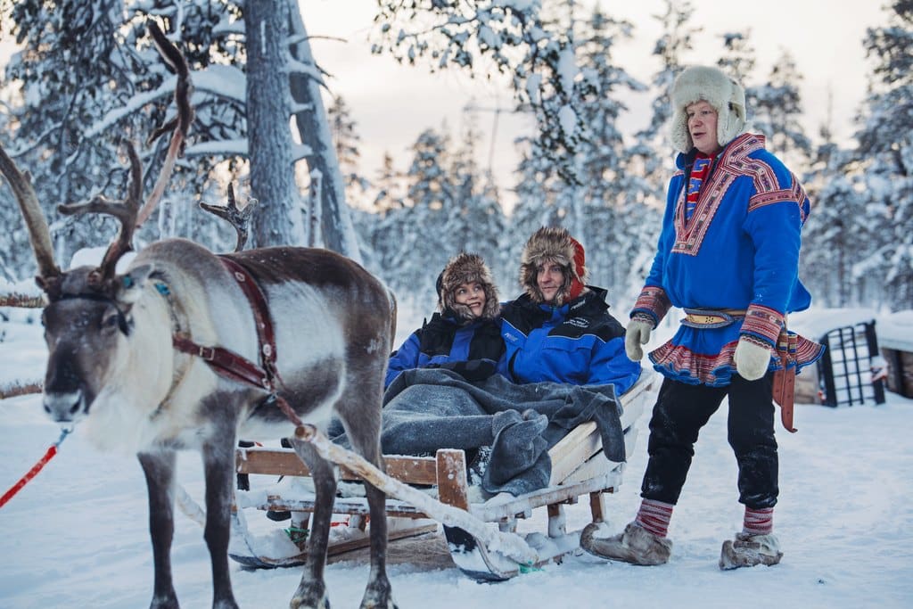 sami man with a reindeer and 2 people sat in the reindeer sleigh