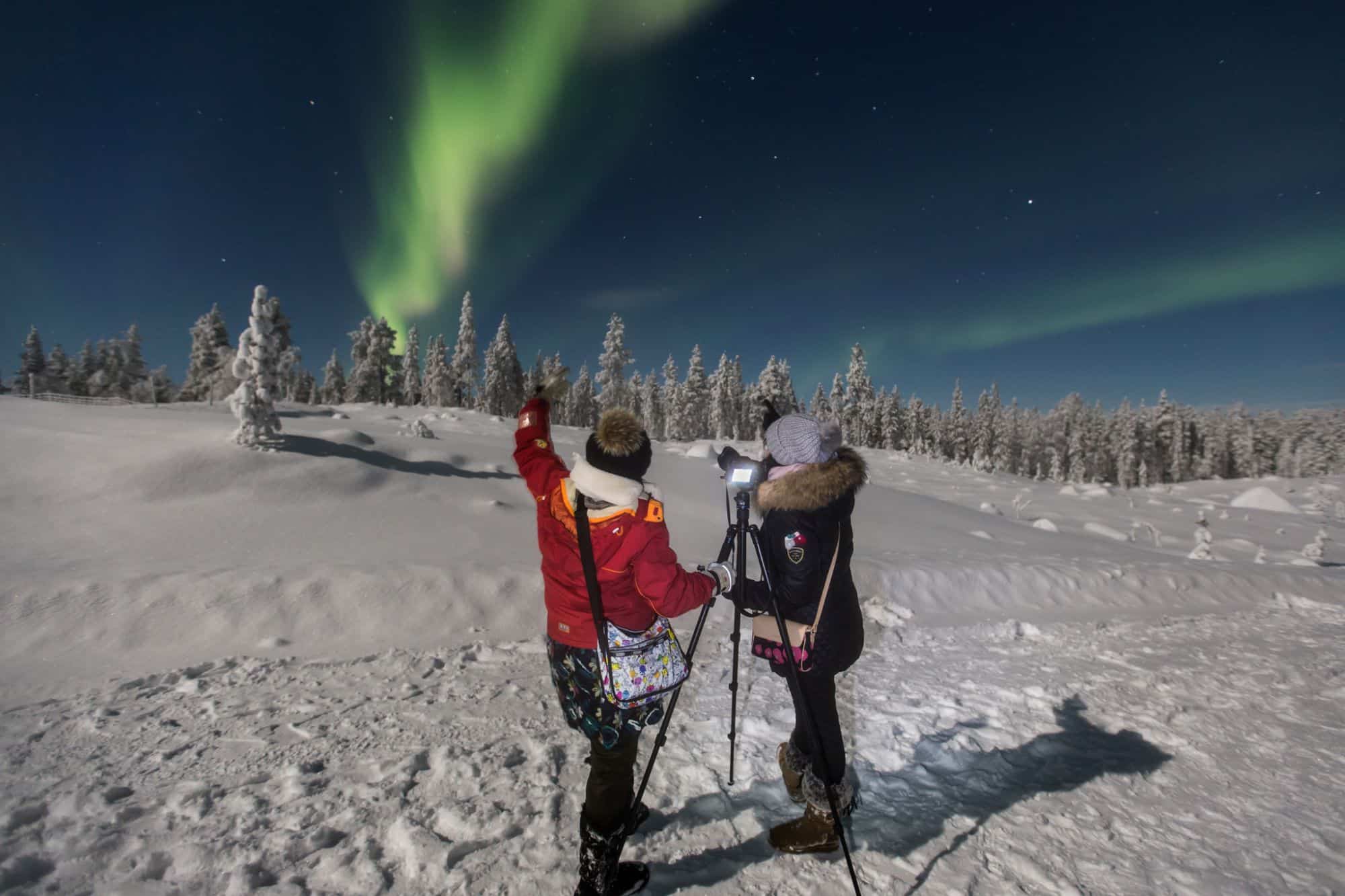 2 people stood in the snow looking at the northern lights