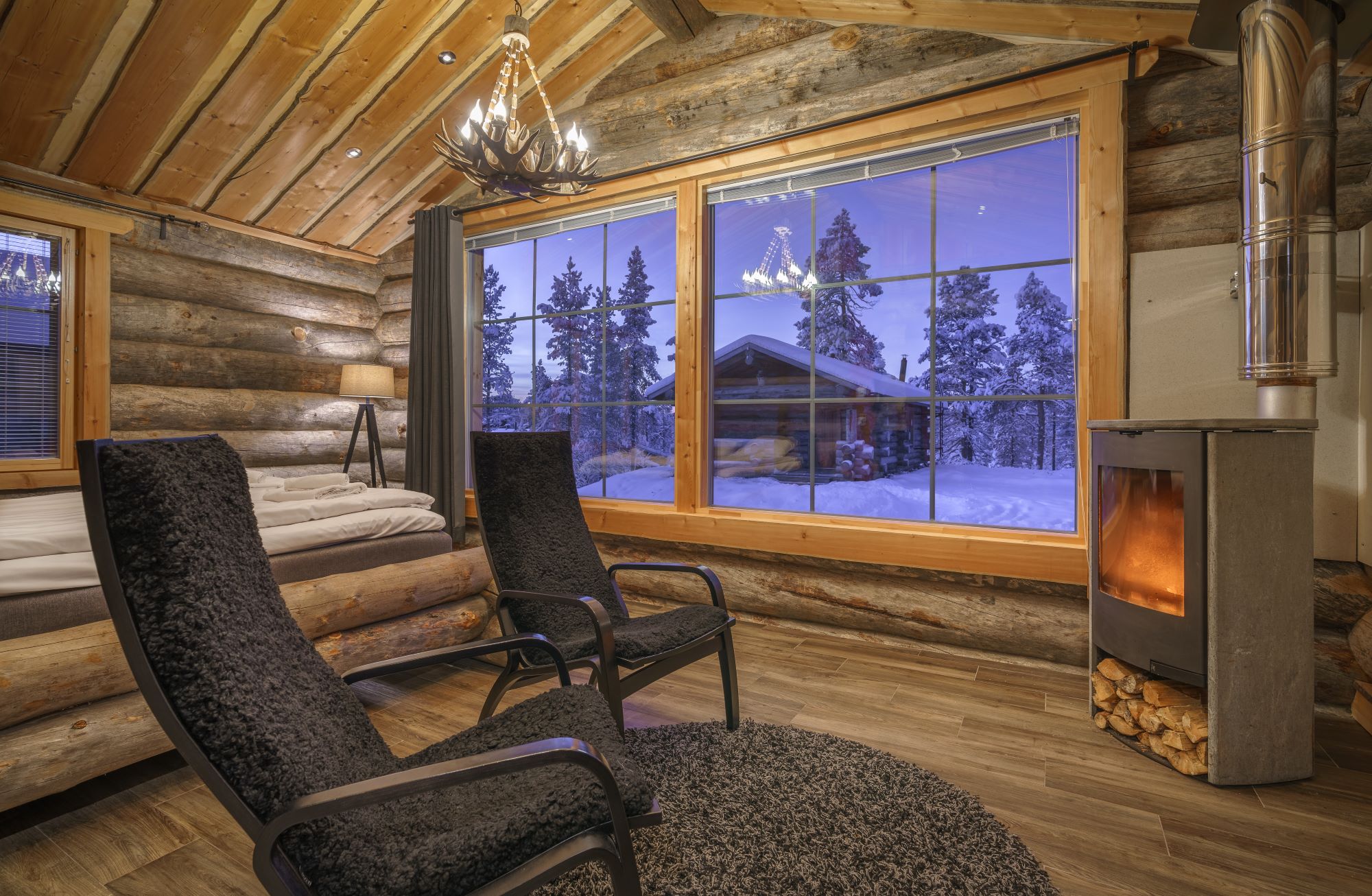 inside log cabin with log burner and 2 chairs infront and view out the window