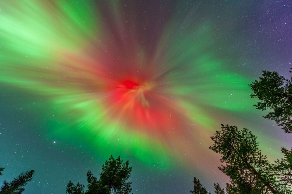 Bright aurora Borealis overhead with green and red hues in a dark sky