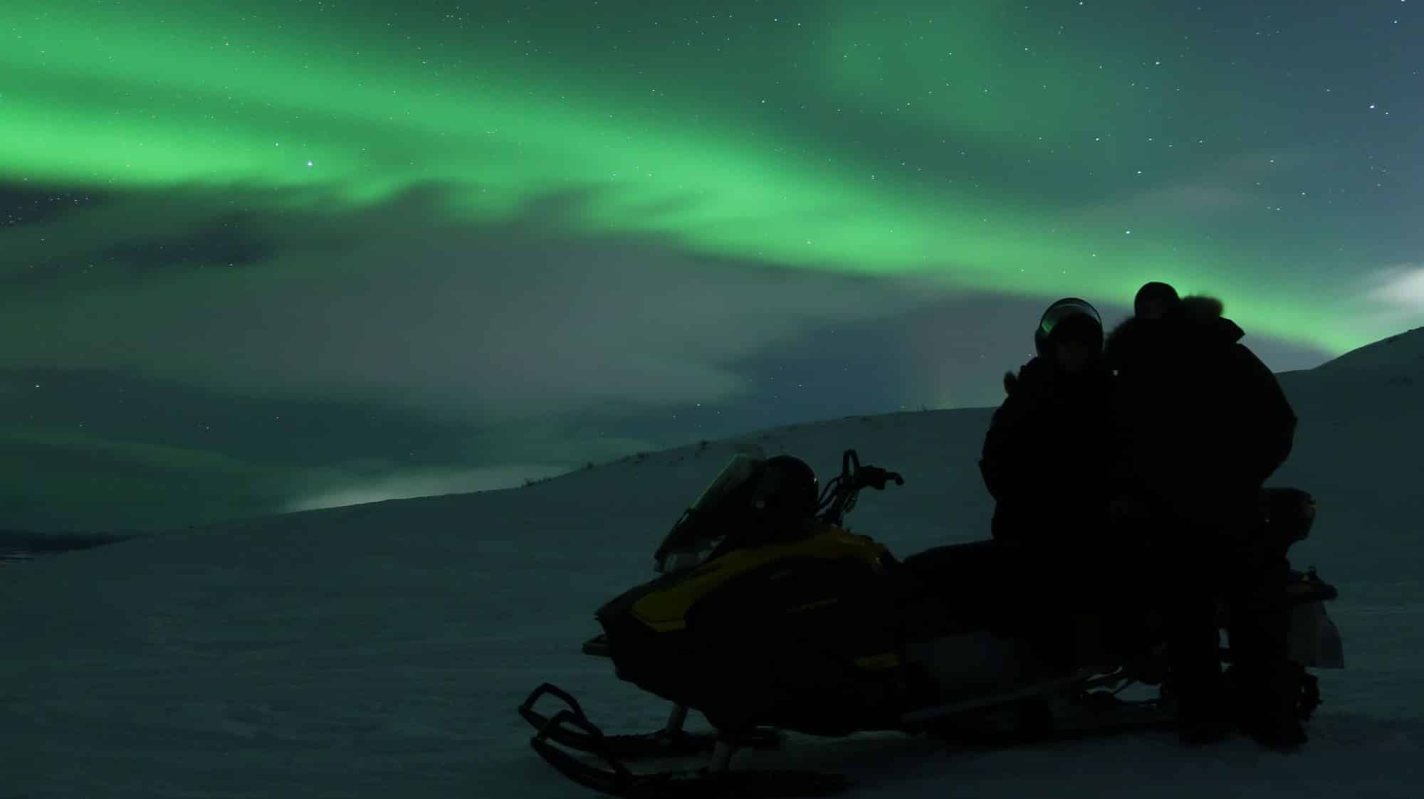 shadow of 2 people on snowmobile with northern lights behind