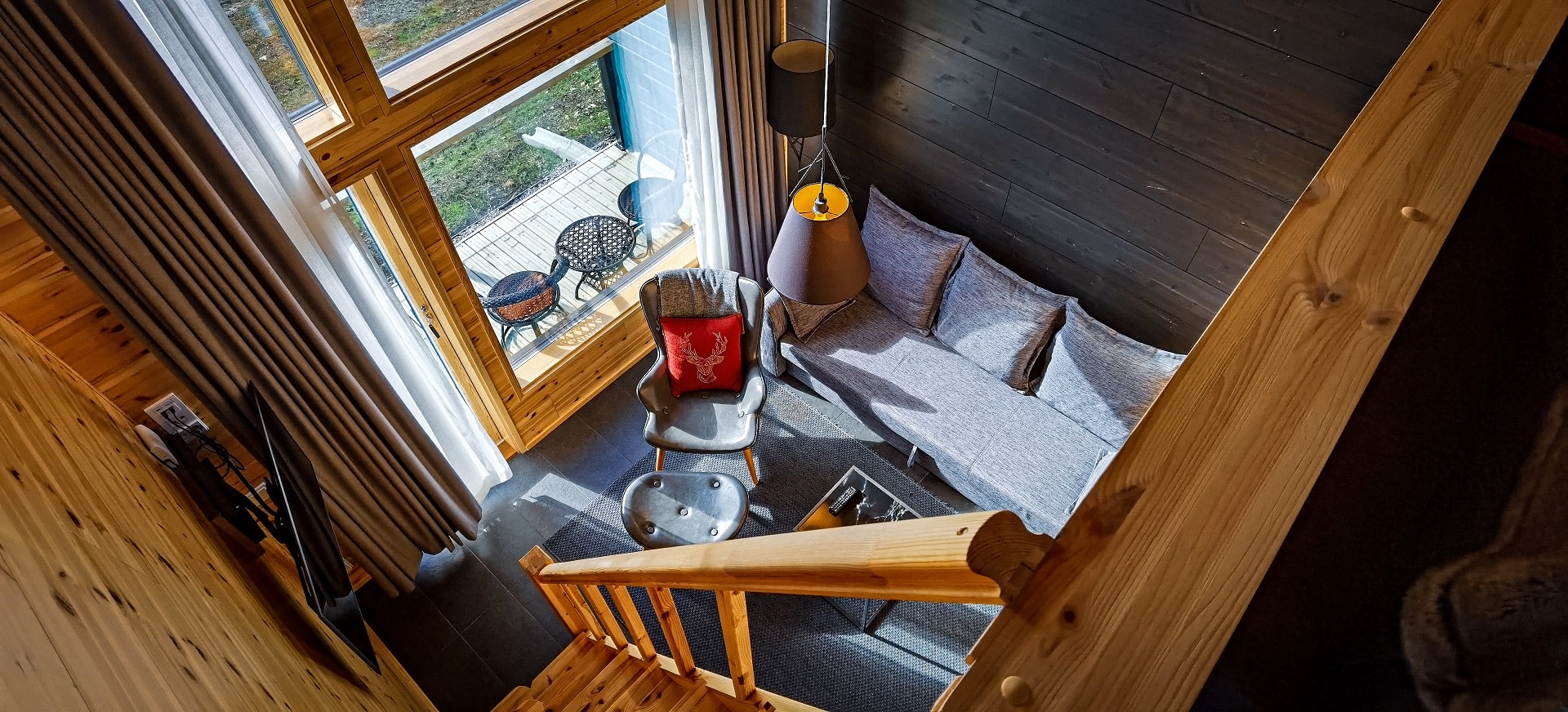Cabin living area with sofa and large window, viewed from the top of wooden stairs.