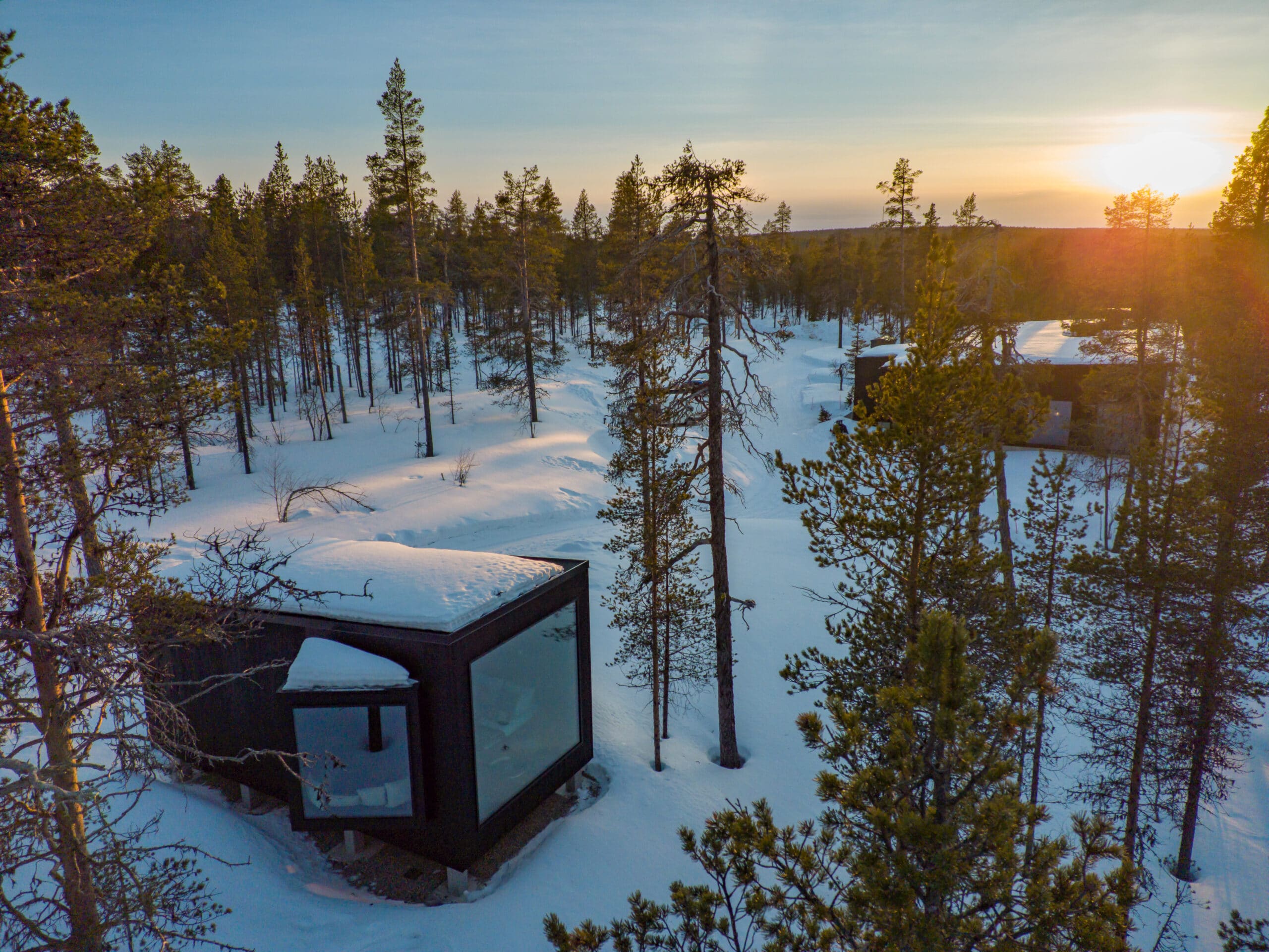 sunset shining through the forest with arctic cabins