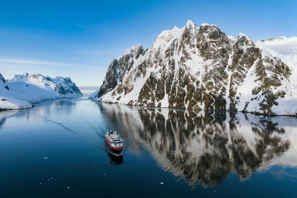 HX Expedition ship cruising through a narrow icy channel with snow-covered mountains