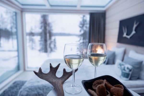 Champagne glasses and snacks on a table inside a glass villa with snowy view outside