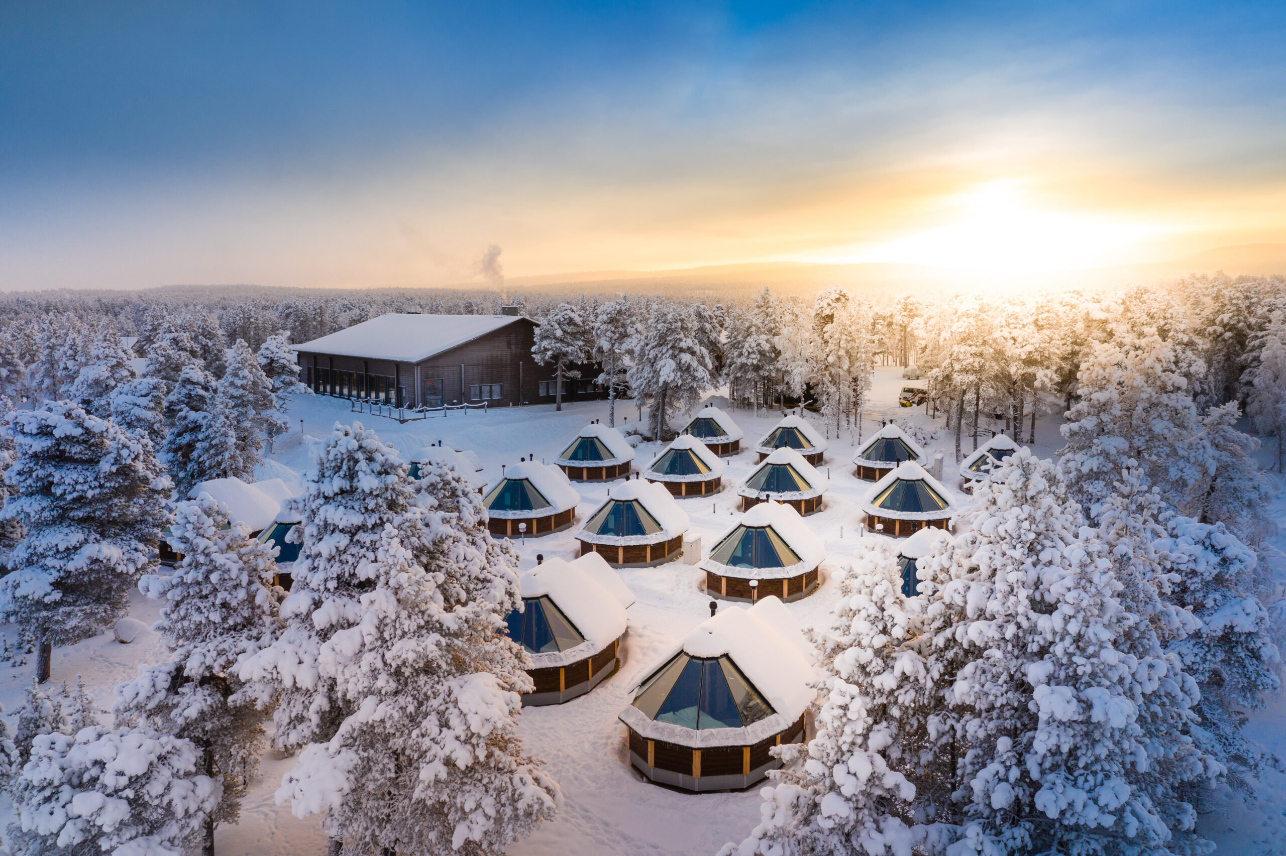Aerial view of snowy resort with glass-roof cabins and warm sunrise light