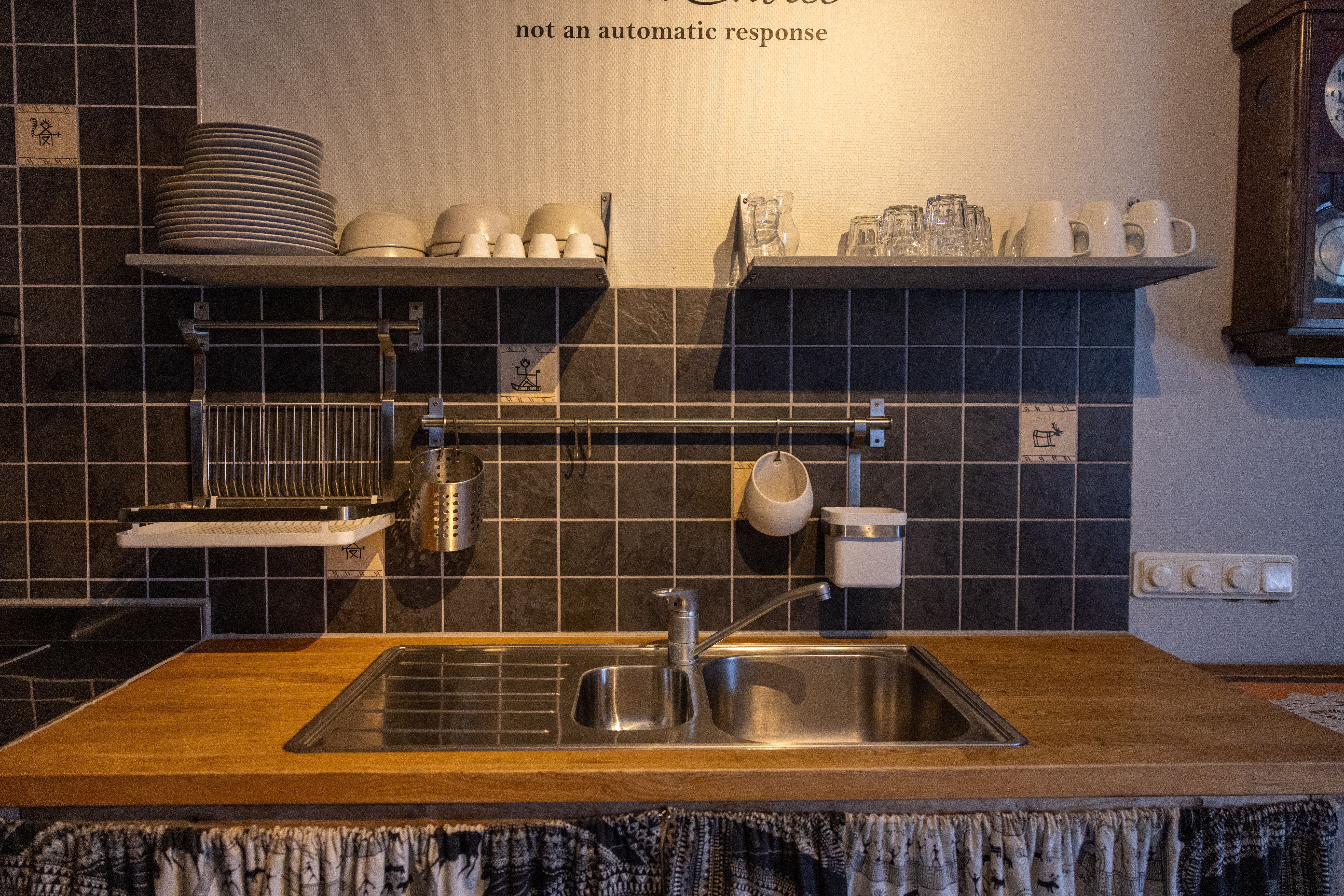 Rustic kitchen sink area with tiled backsplash, shelves of cups and plates