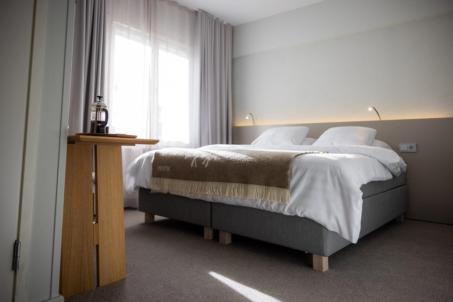 Modern hotel room with double bed, grey headboard, armchair and large window