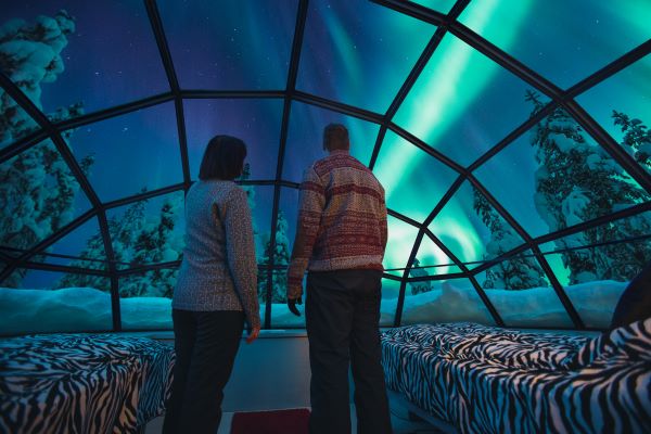 couple stoof in glass igloo watching the northern lights