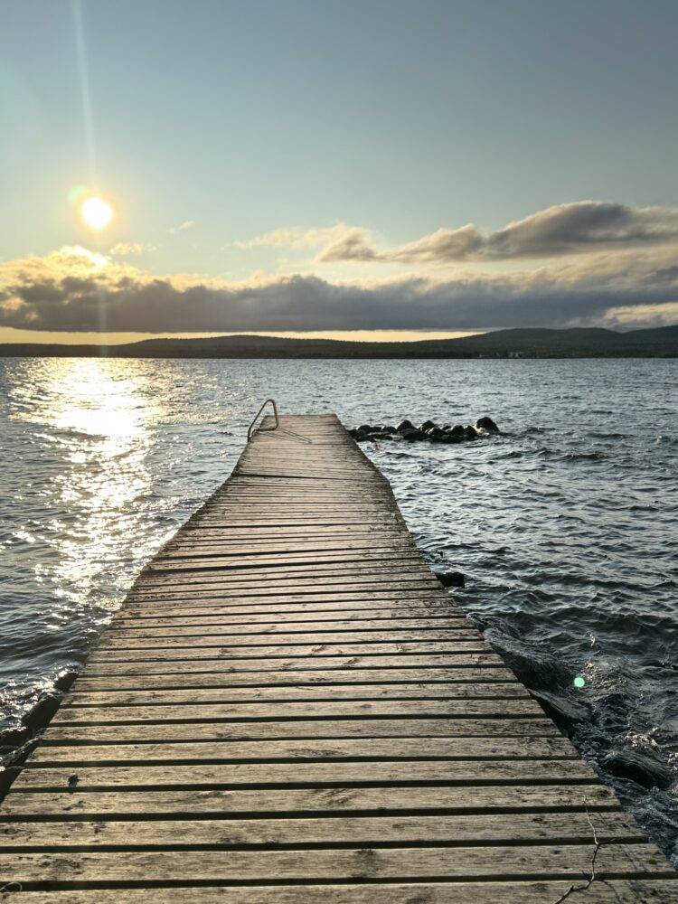 Wooden jetty leading into a calm lake at sunset with warm orange sky