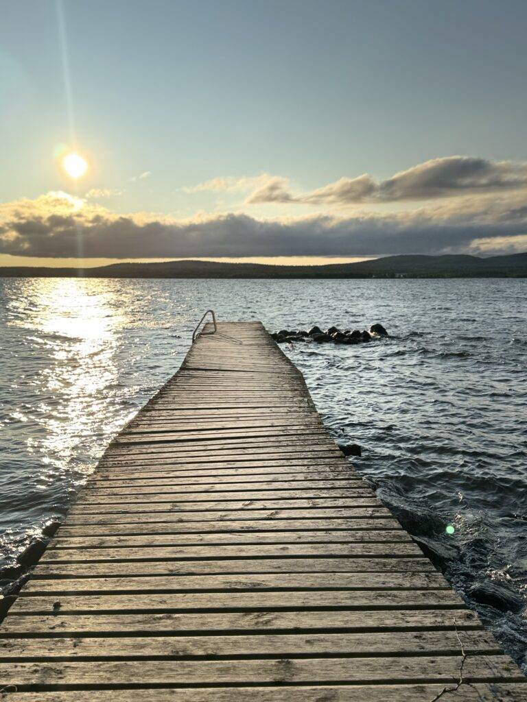 Wooden jetty leading into a calm lake at sunset with warm orange sky