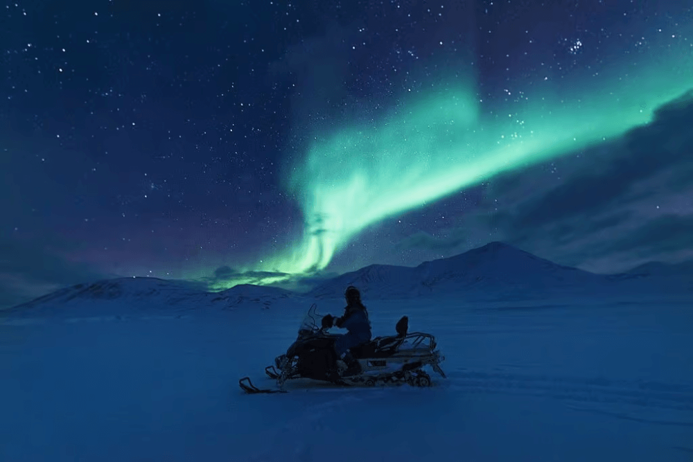 person snowmobiling with northern lights above