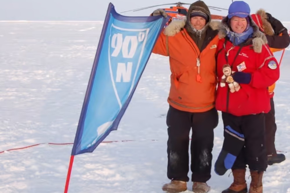2 people stood with flag in the north pole