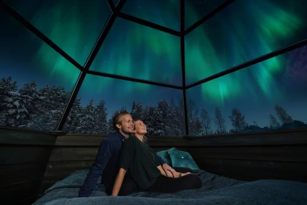 couple sat in glass igloo with northern lights above