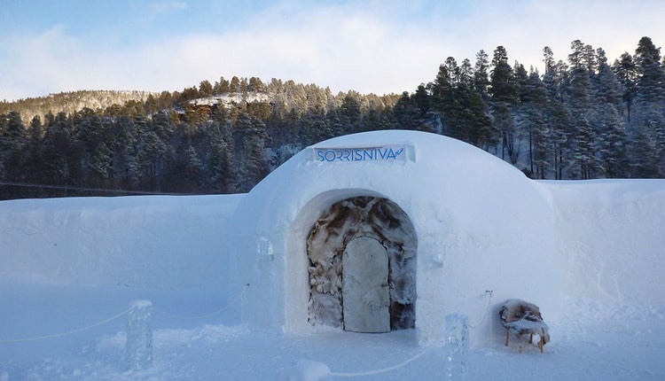 Entrance to the Sorrisniva ice hotel, a white snow dome with an arched doorway in a winter forest