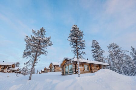 Row of wooden log cabins in snowy woodland under a pale winter sky