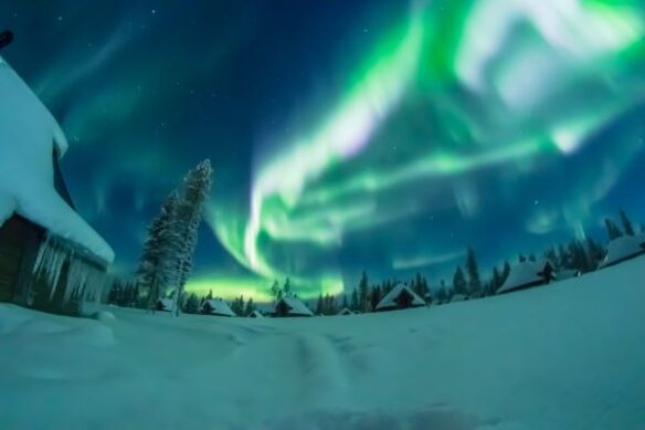Northern lights over a snowy village at night with warm lights in the buildings below