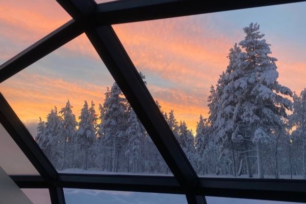 sunset and snowy forest through the glass igloo window