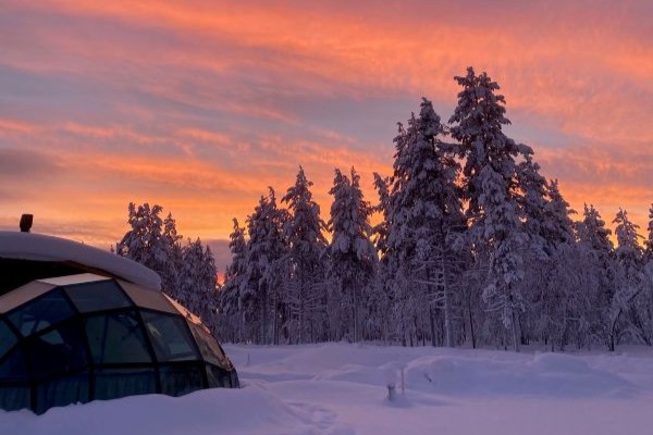 glass igloo with red sky and snow covered trees in finland