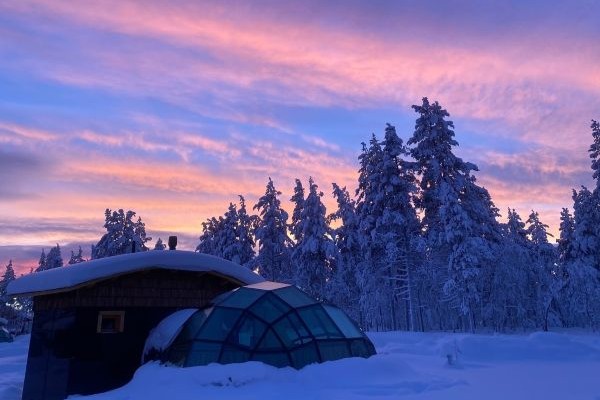 glass igloo covered in snow with sunset behind