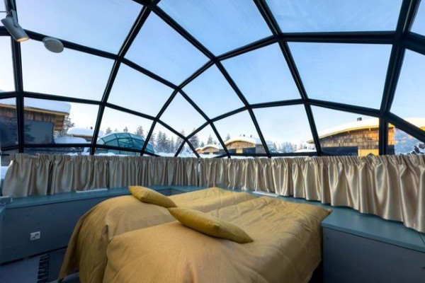 double bed inside glass igloo with blue skies behind